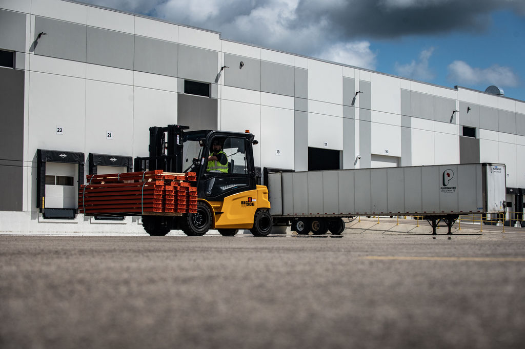 Big Joe forklift moving bundled racking beside a trailer outside a warehouse
